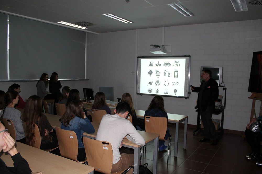 W zaciemnionej sali seminaryjnej grupa studentów ogląda wykład na dużym ekranie